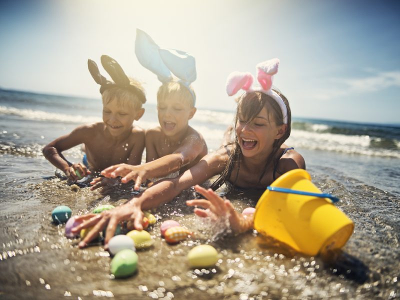 Summer easter on beach. Kids aged 8 and 11 are lying in sea water and having fun wearing easter bunny ears. Kids are catching easter eggs in water.