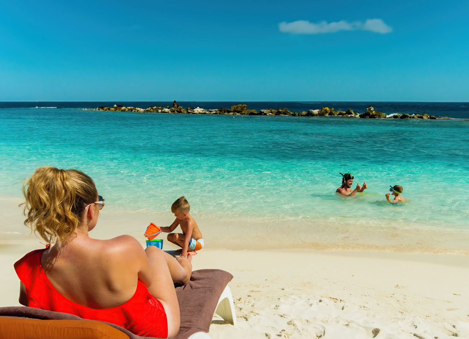 Woman resting at the beach while a man and children play together