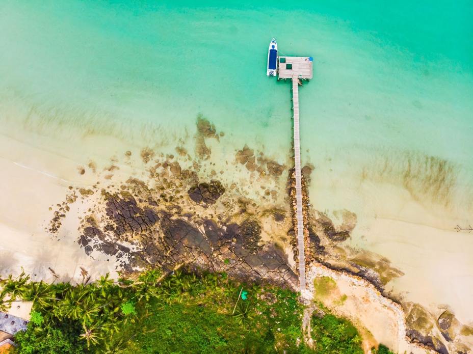 Aerial view from the sea with a pier, a boat and some rocks nearby