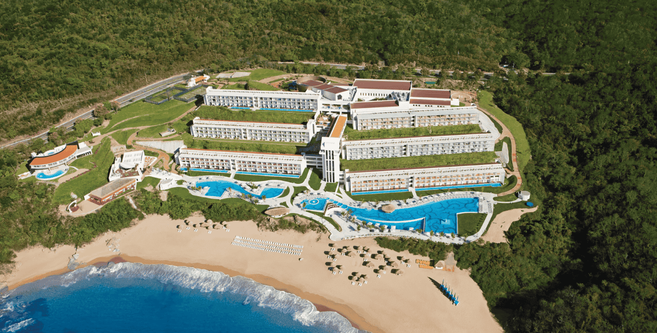 aerial view of a seaside resort surrounded by mountains and lush vegetation. secrets huatulco resort & spa.