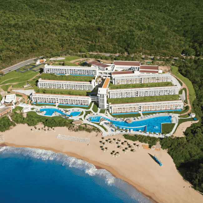 aerial view of a seaside resort surrounded by mountains and lush vegetation. secrets huatulco resort & spa.
