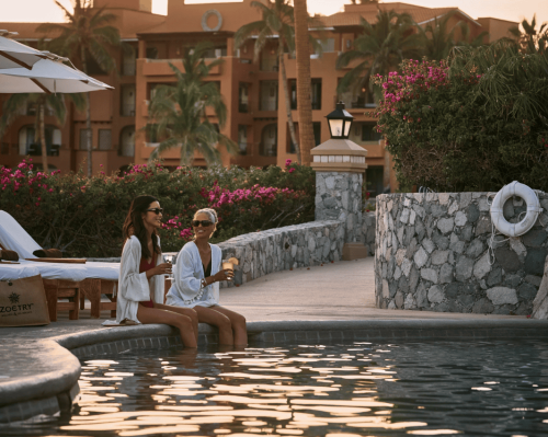 two women relaxing by resort pool at sunset with cocktails zoëtry casa del mar los cabos